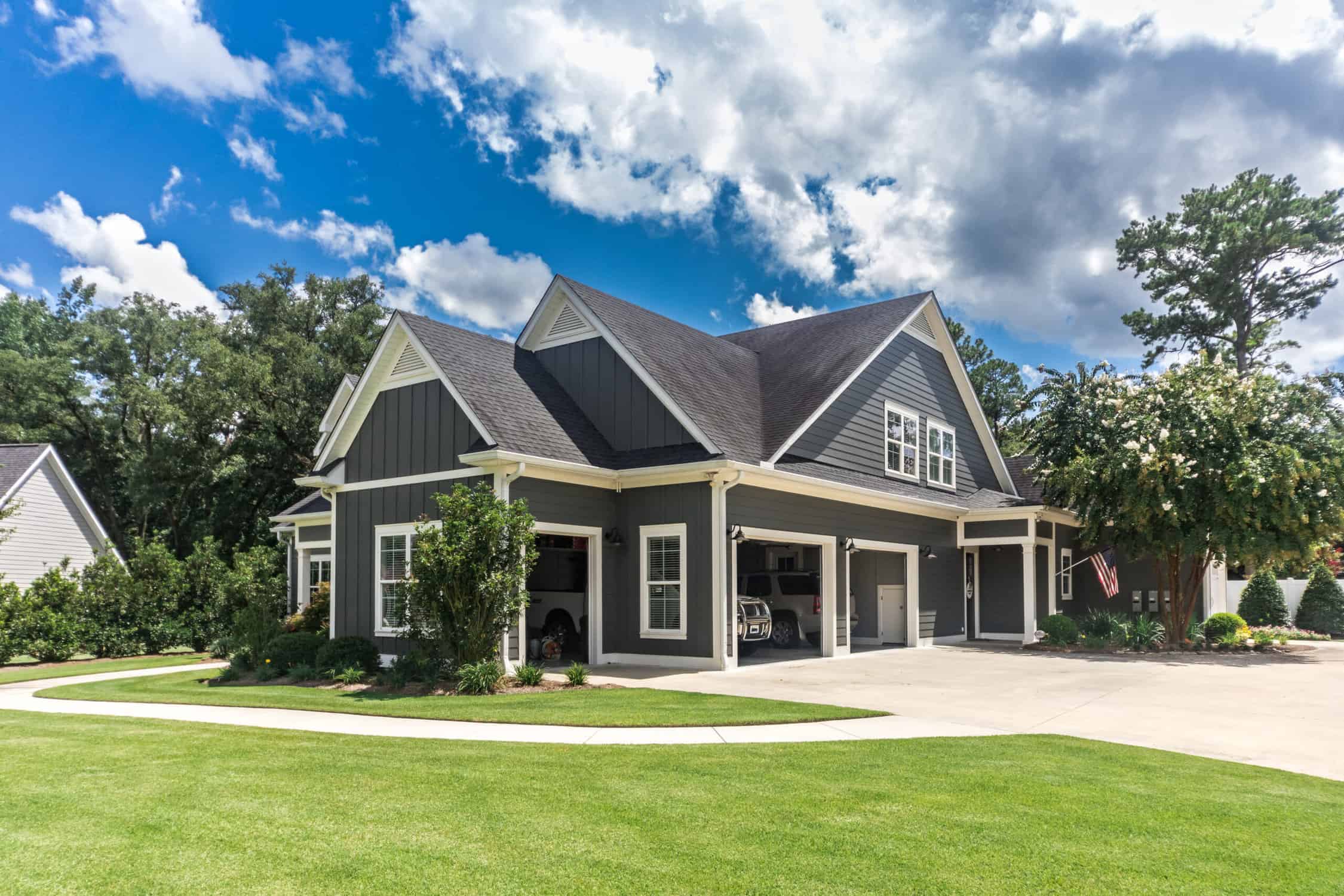 The side view of a large gray craftsman new construction house with a landscaped yard a three car garage and driveway The side view of a large gray craftsman new construction house with a landscaped yard a three car garage and driveway.