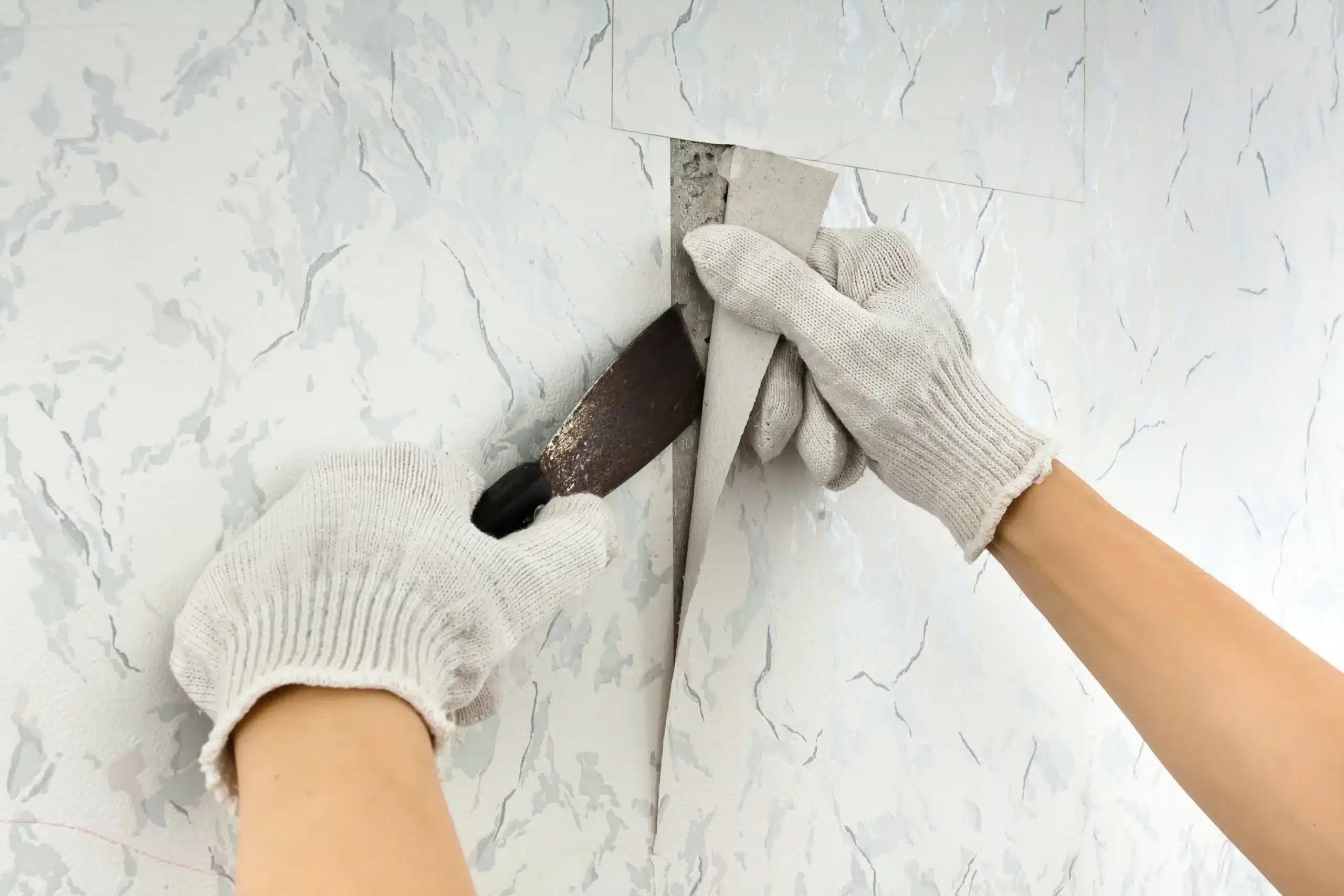 Efficient Wallpaper Removal Services in Simi Valley California Gloved hands carefully scrape and remove old wallpaper from a wall in Simi Valley California.