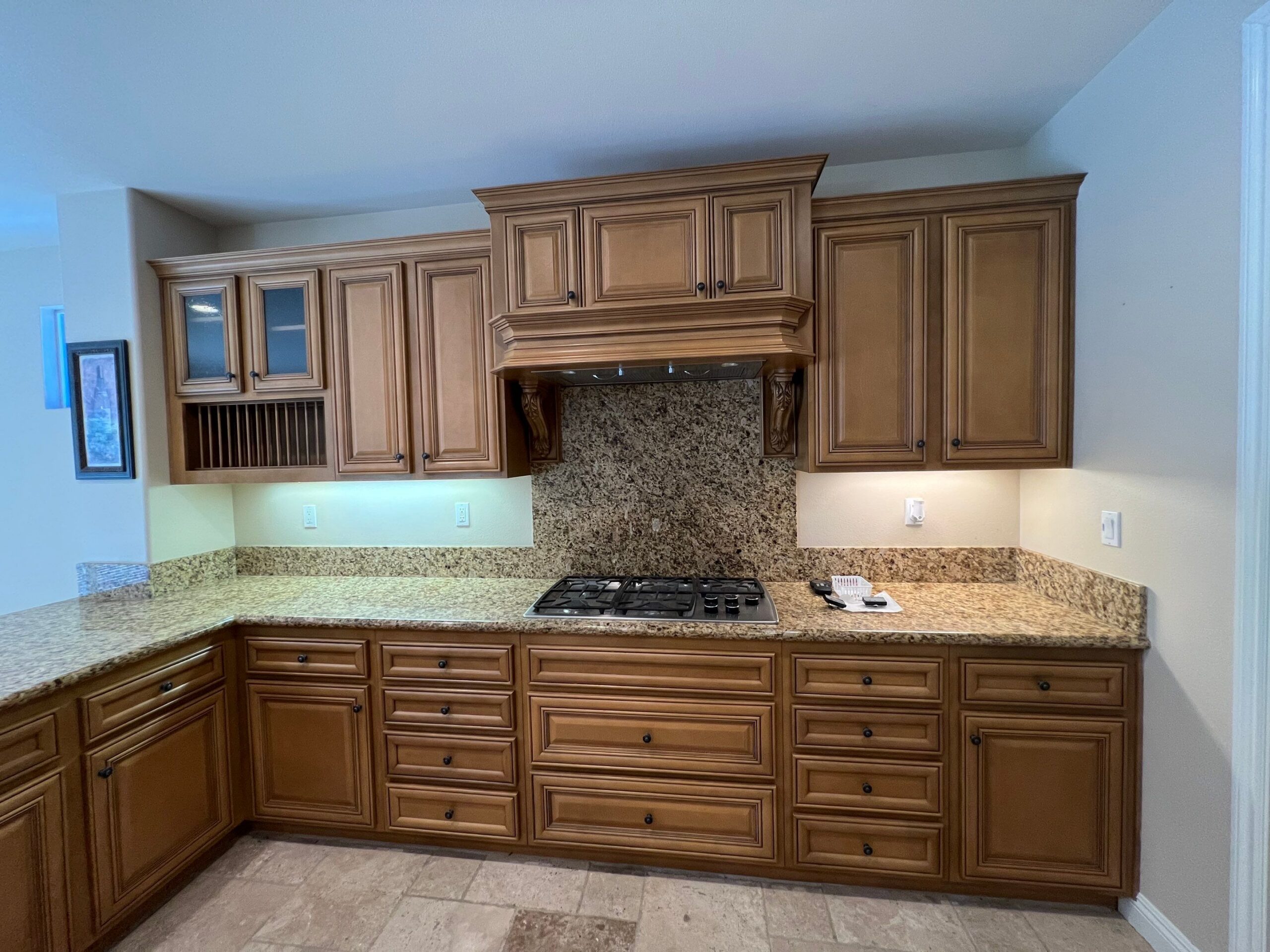 Warm Walnut Kitchen Cabinets Warm walnut-stained kitchen cabinets with granite countertops, speckled backsplash, and gas cooktop in residential kitchen