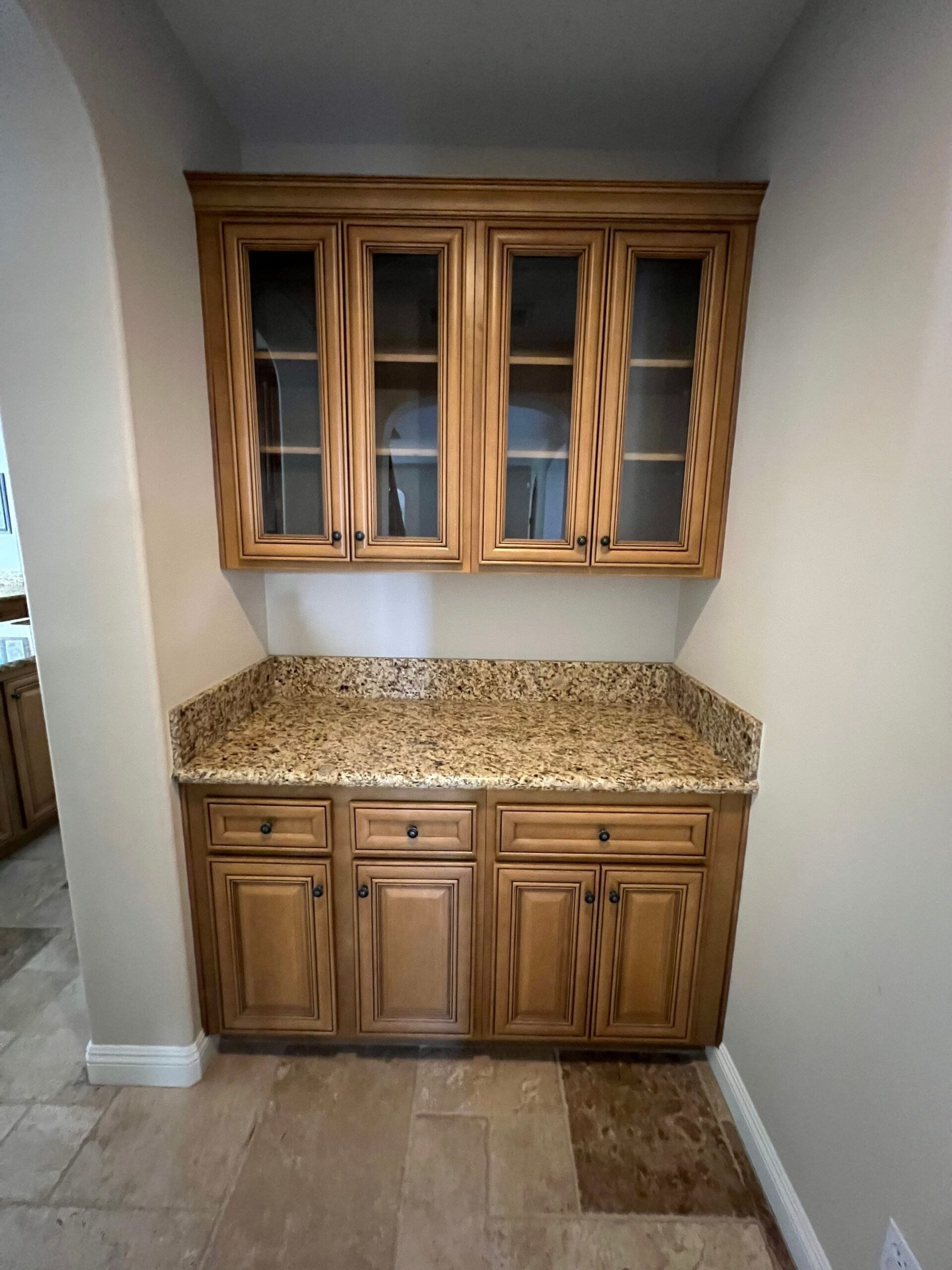 Walnut Stained Kitchen Cabinets Walnut-stained kitchen cabinetry with glass-door upper cabinets, granite countertop, and white walls in residential interior