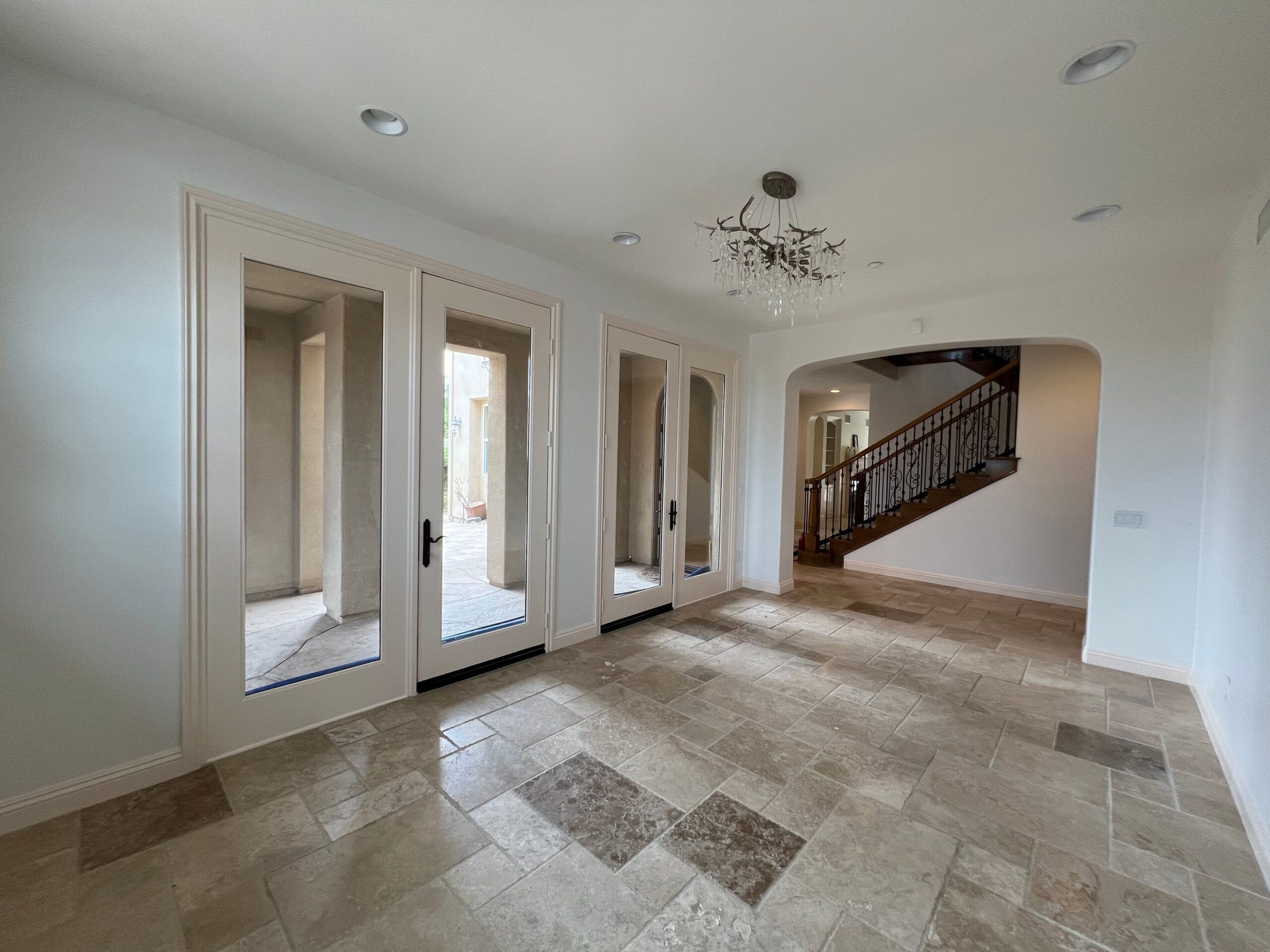 Cream Interior Residential Home Entry Cream-painted interior entryway with white trim, glass-door closets, travertine tile flooring, and staircase opening in