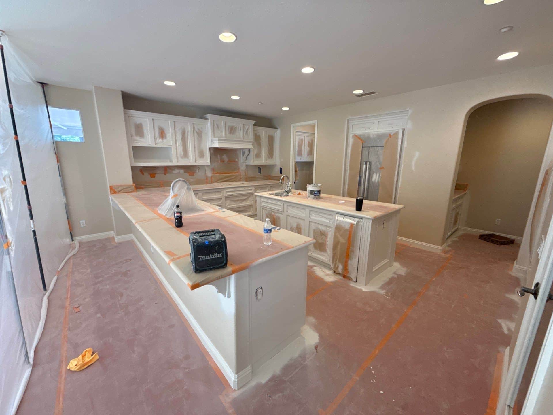 Kitchen Cabinet Painting Project Cream-painted kitchen cabinetry with white trim, center islands, granite countertops, and protective coverings during